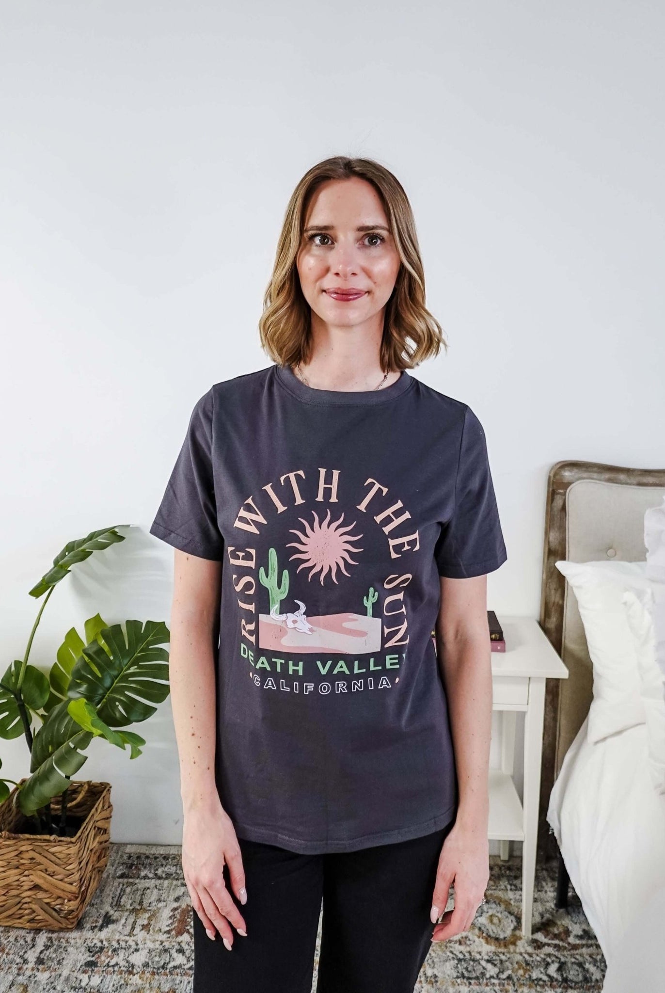 women wearing a dark grey graphic t-shirt with the saying rise with the sun death valley california