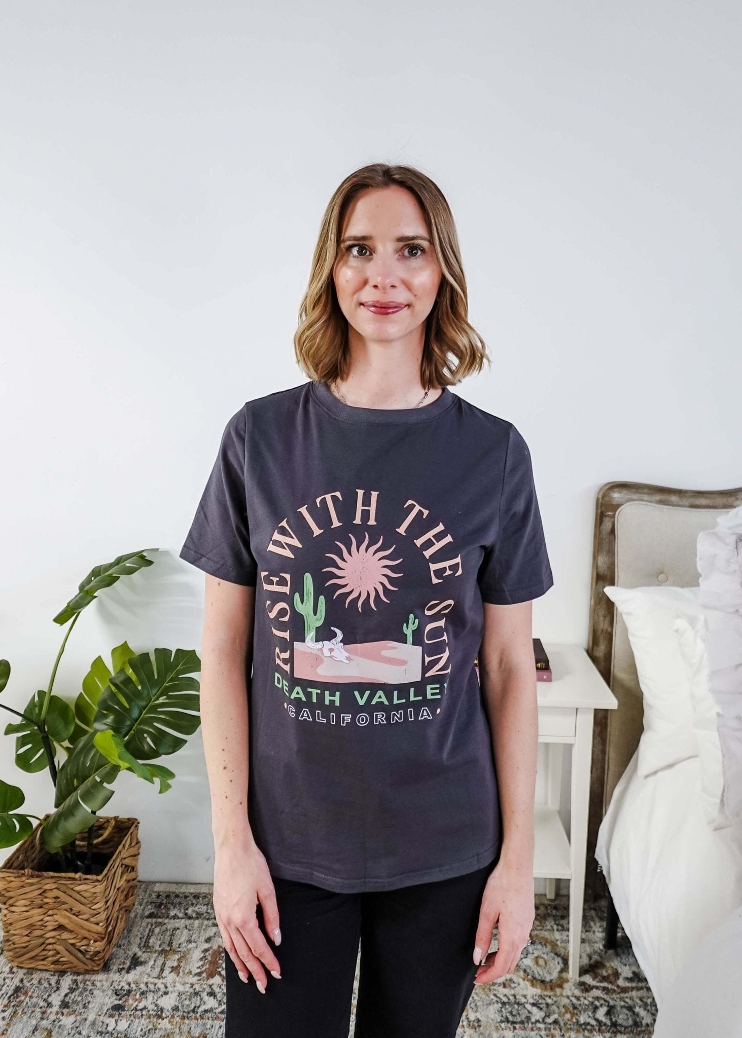 women wearing a dark grey graphic t-shirt with the saying rise with the sun death valley california