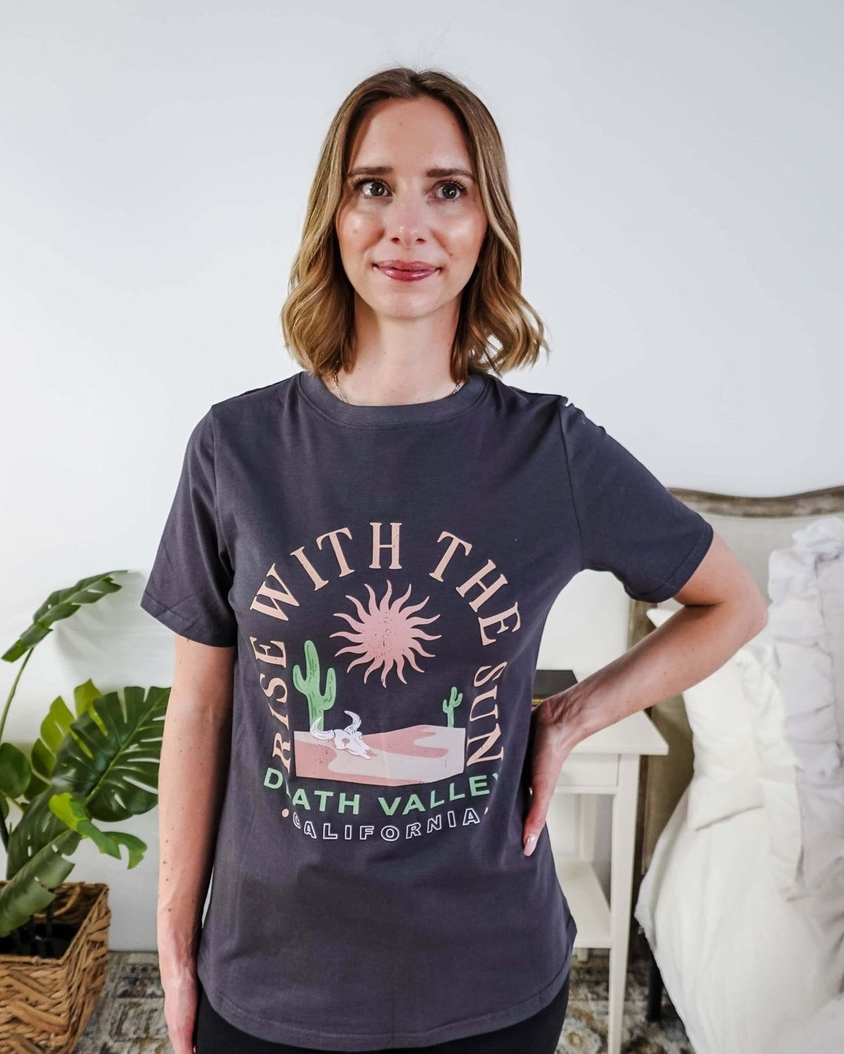 women wearing a dark grey graphic t-shirt with the saying rise with the sun death valley california