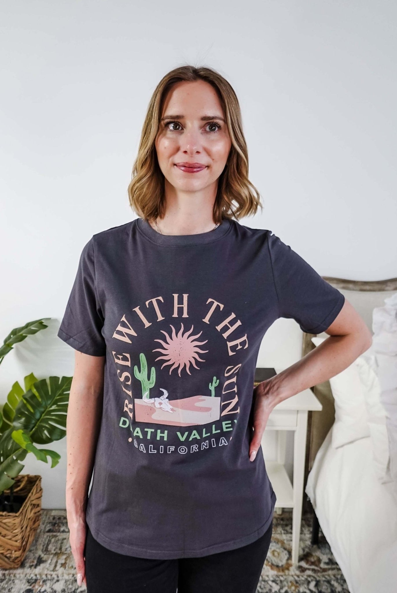 women wearing a dark grey graphic t-shirt with the saying rise with the sun death valley california