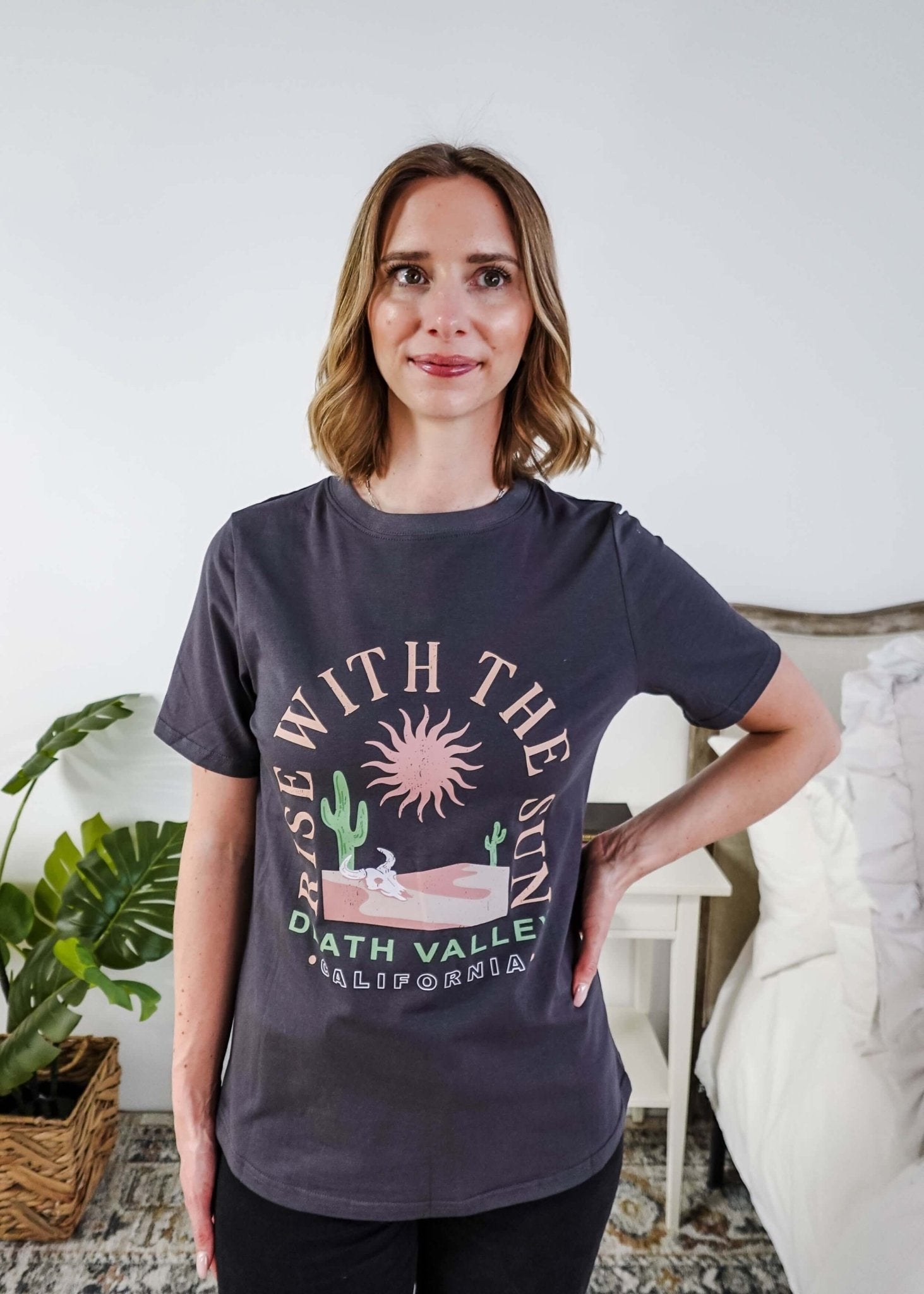 women wearing a dark grey graphic t-shirt with the saying rise with the sun death valley california