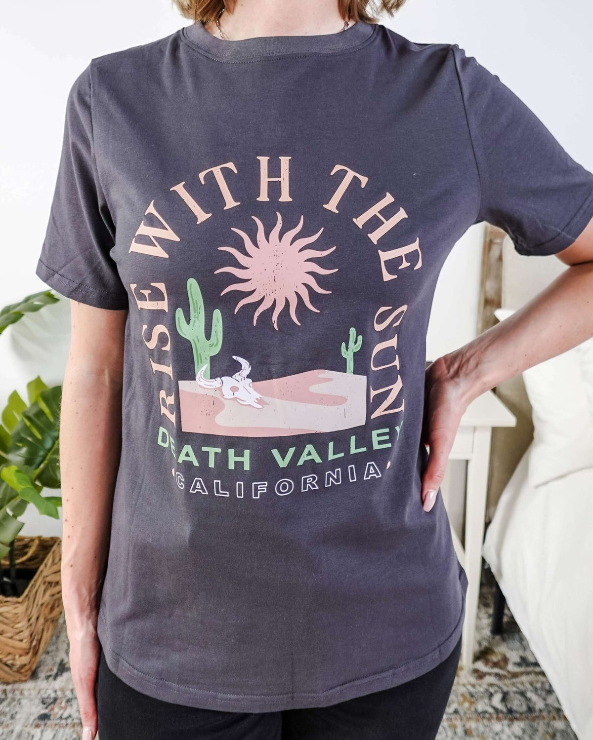 women wearing a dark grey graphic t-shirt with the saying rise with the sun death valley california