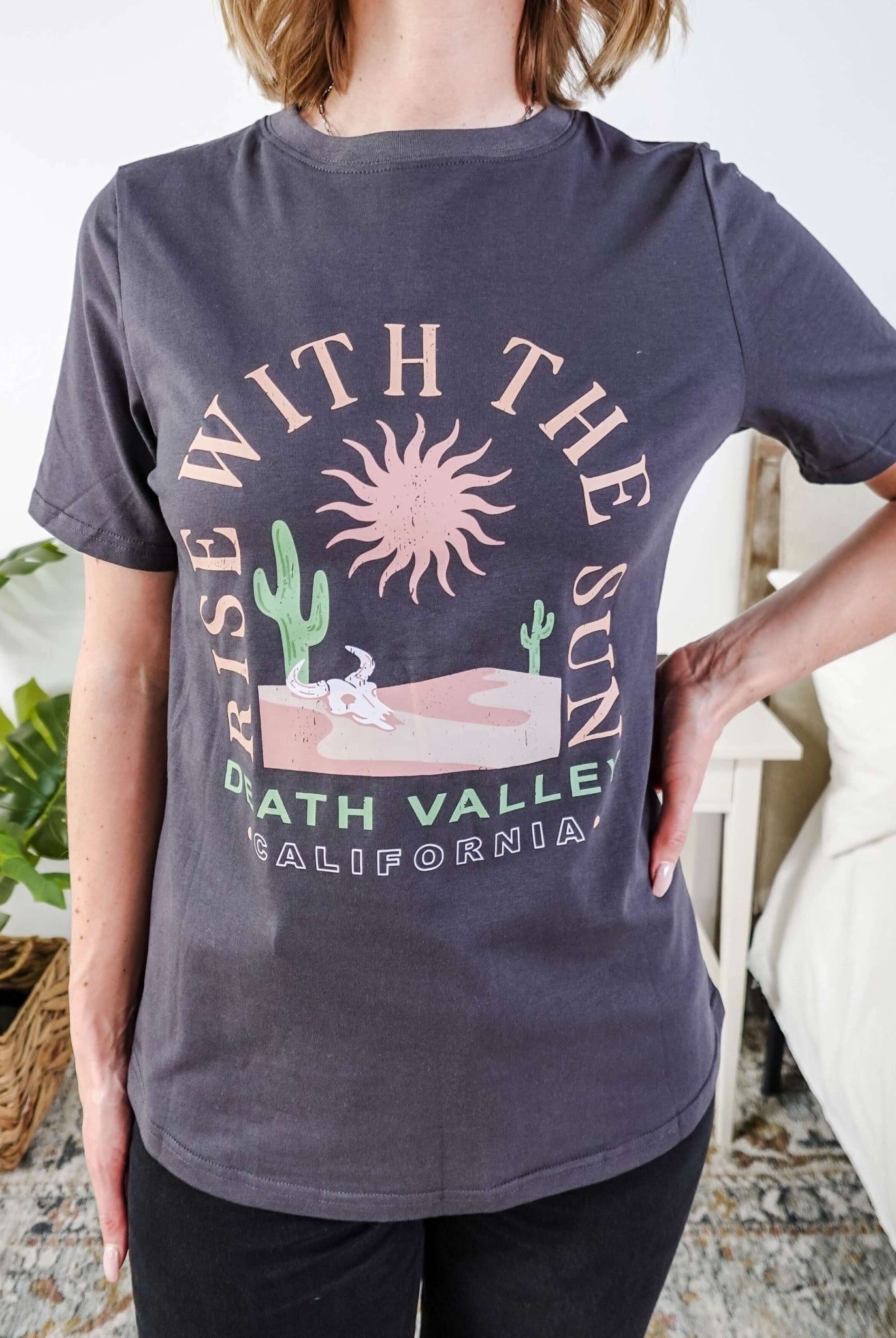 women wearing a dark grey graphic t-shirt with the saying rise with the sun death valley california