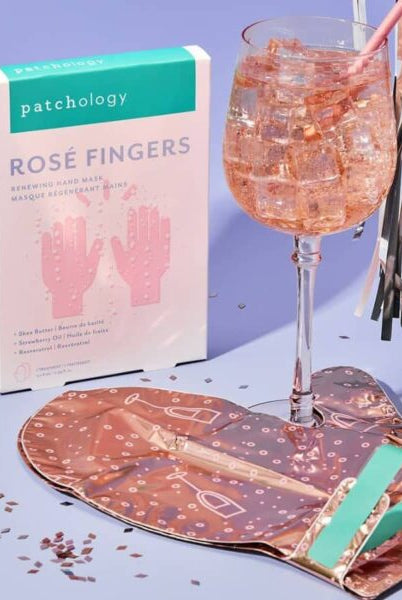 Patchology Rosé Fingers product with a glass of rosé and a patterned bag on a blue background, Patchology Rosé Fingers renewing hand mask rose gold gloves shea butter