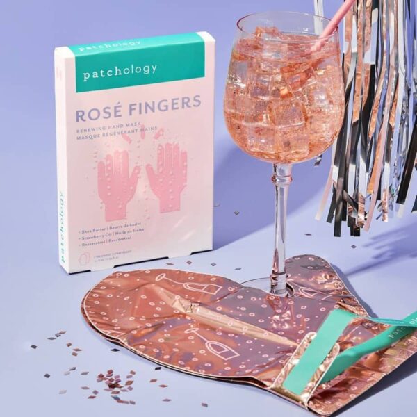 Patchology Rosé Fingers product with a glass of rosé and a patterned bag on a blue background, Patchology Rosé Fingers renewing hand mask rose gold gloves shea butter