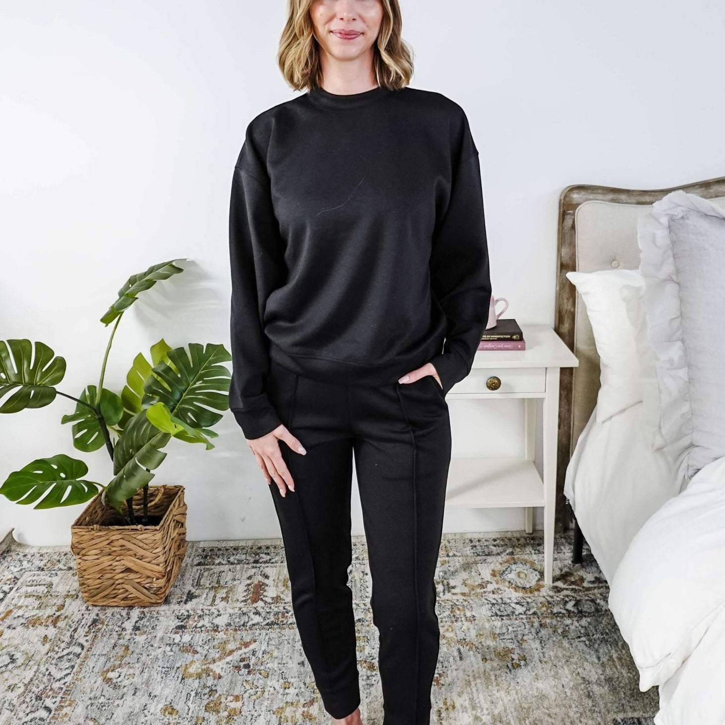 Woman wearing a black lounge outfit standing in a bedroom.