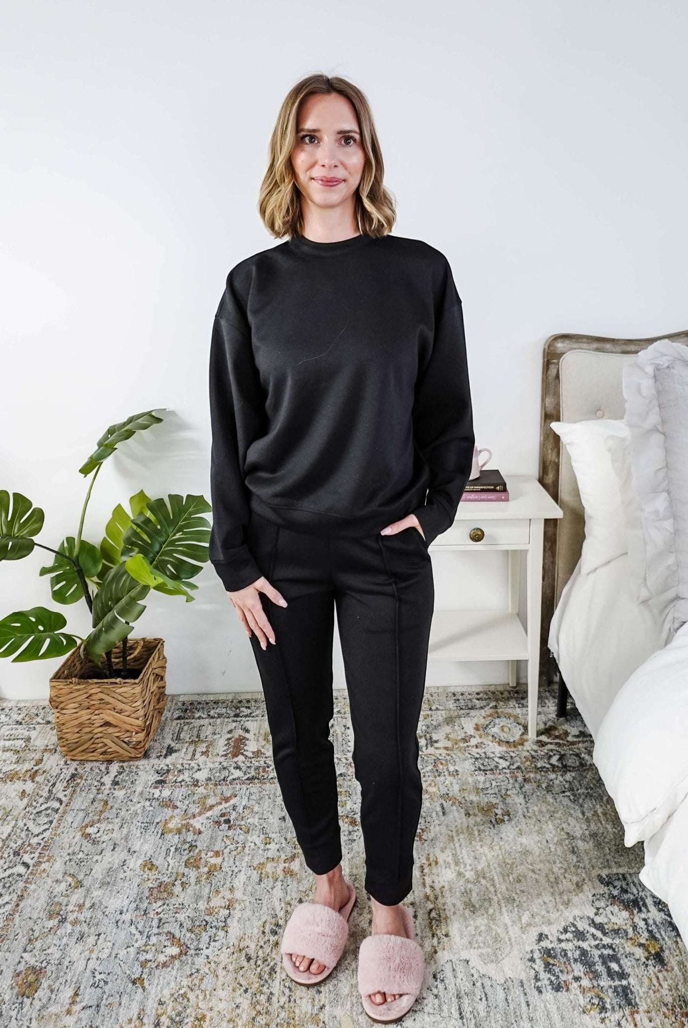 Woman wearing a black lounge outfit standing in a bedroom.