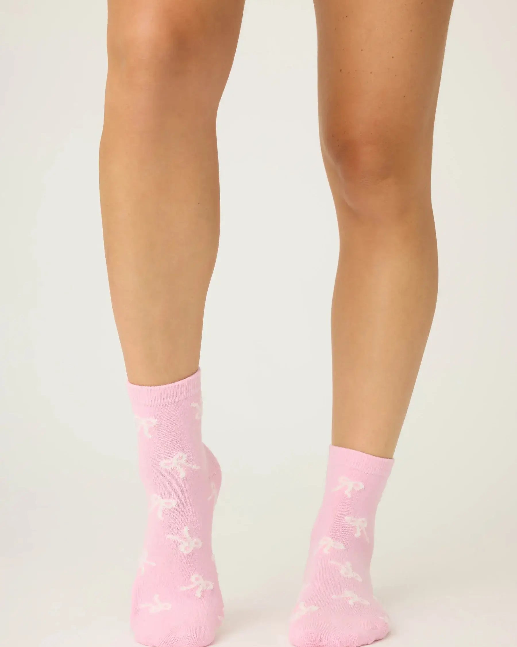 Pair of PJ Salvage Bright Pink Fuzzy Crew Socks with a whimsical all-over white bow print. Showing the plush texture and grip soles.