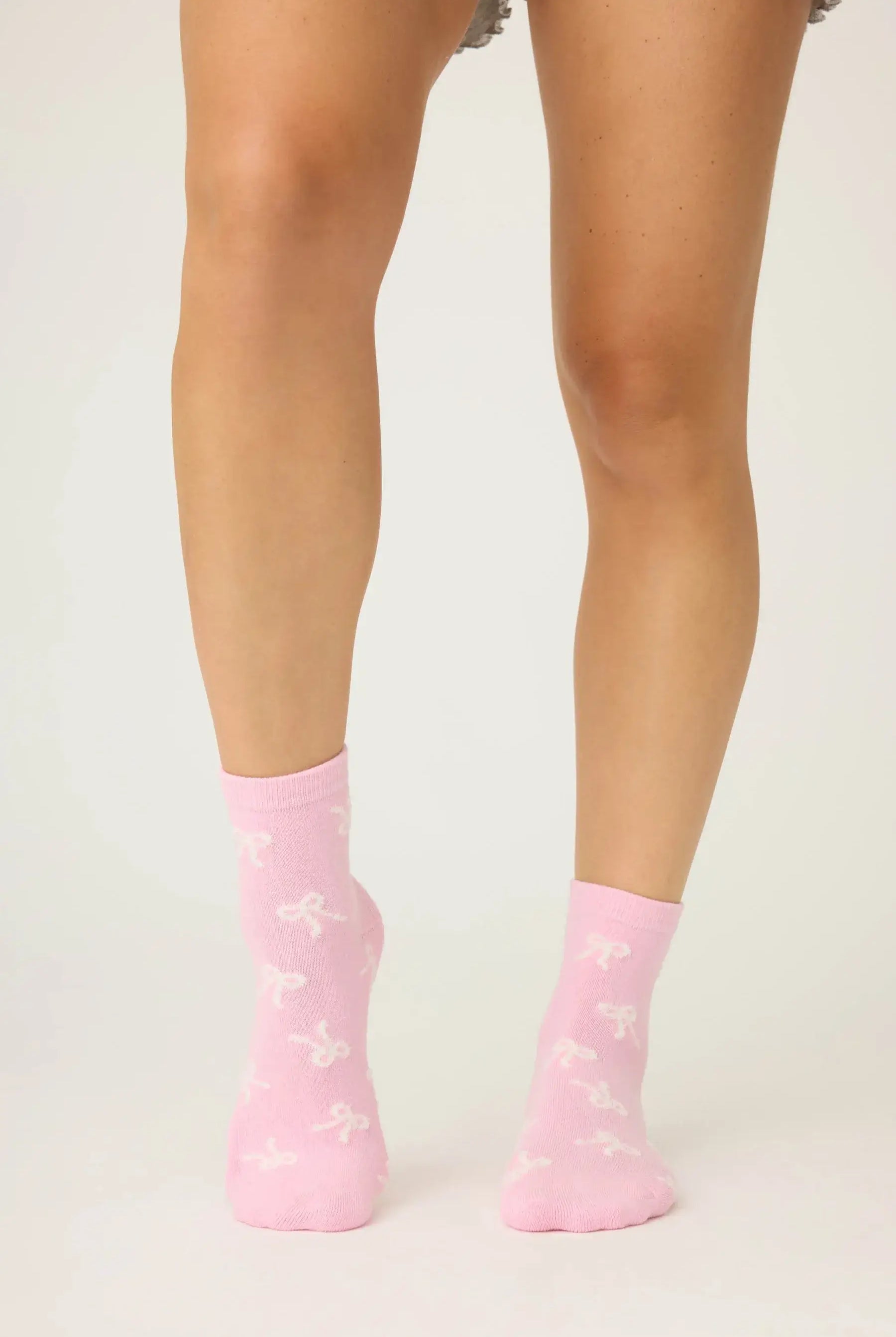 Pair of PJ Salvage Bright Pink Fuzzy Crew Socks with a whimsical all-over white bow print. Showing the plush texture and grip soles.
