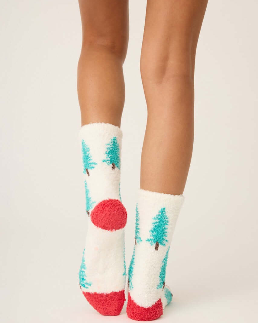 Pair of PJ Salvage "Sleigh All Day" Fuzzy Cozy Socks in ivory with green tree print and red heel, showing the anti-skid grippers on the sole.