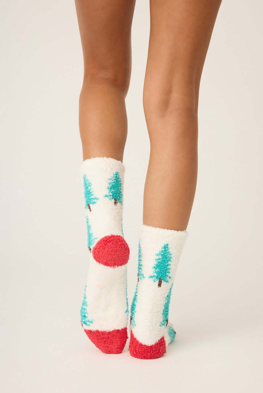 Pair of PJ Salvage "Sleigh All Day" Fuzzy Cozy Socks in ivory with green tree print and red heel, showing the anti-skid grippers on the sole.