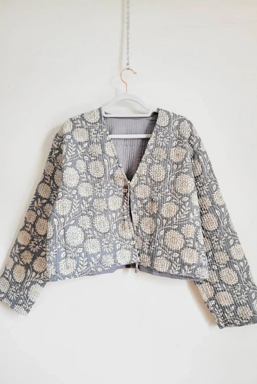 Floral print blue quilted jacket by French Toast Handmade. Hanging from a hanger on a light background