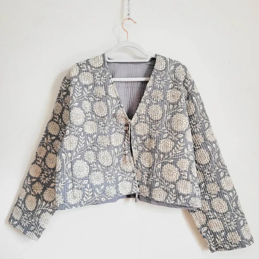 Floral print blue quilted jacket by French Toast Handmade. Hanging from a hanger on a light background