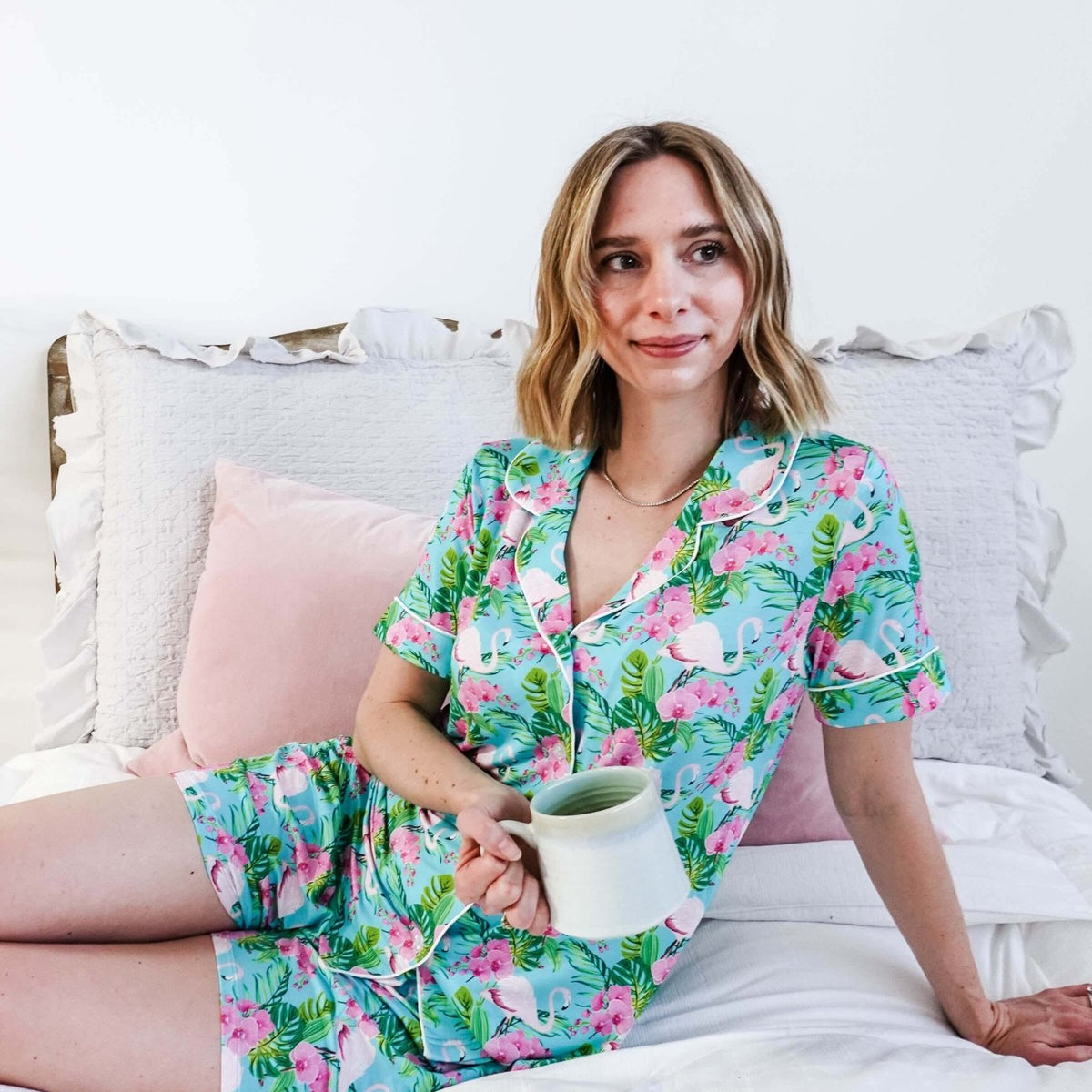 Woman enjoying a coffee in Tropic Like It's Hot Bamboo Short Sleeve Pajama Set by Georgia Rylan on a cozy bed.