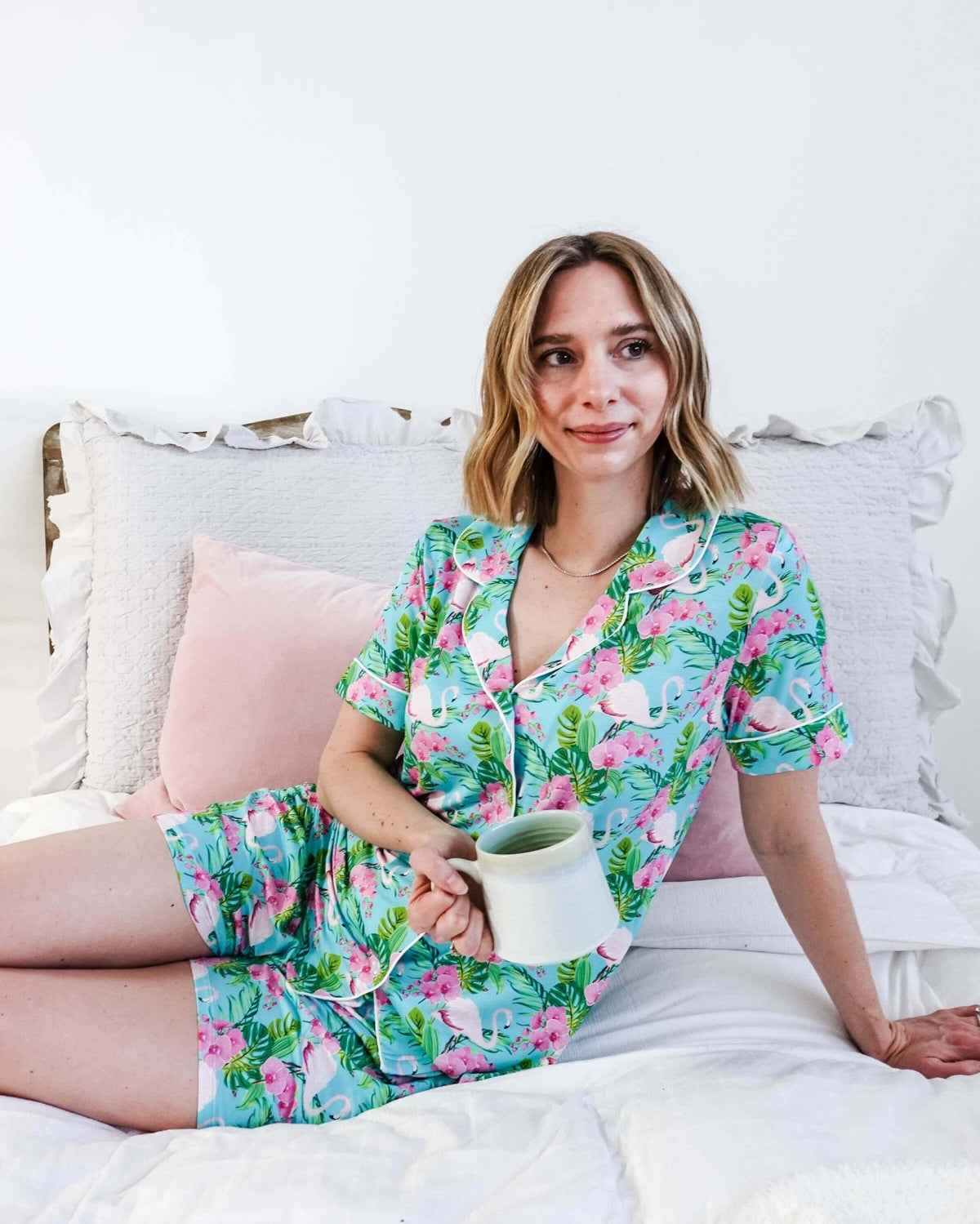 Woman enjoying a coffee in Tropic Like It's Hot Bamboo Short Sleeve Pajama Set by Georgia Rylan on a cozy bed.