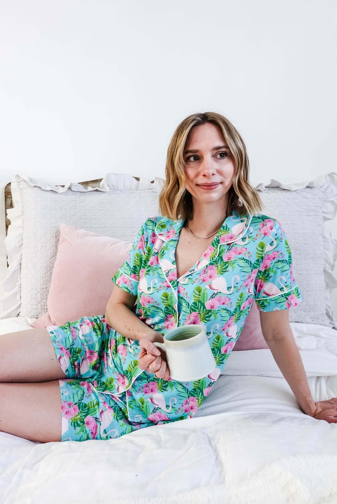 Woman enjoying a coffee in Tropic Like It's Hot Bamboo Short Sleeve Pajama Set by Georgia Rylan on a cozy bed.