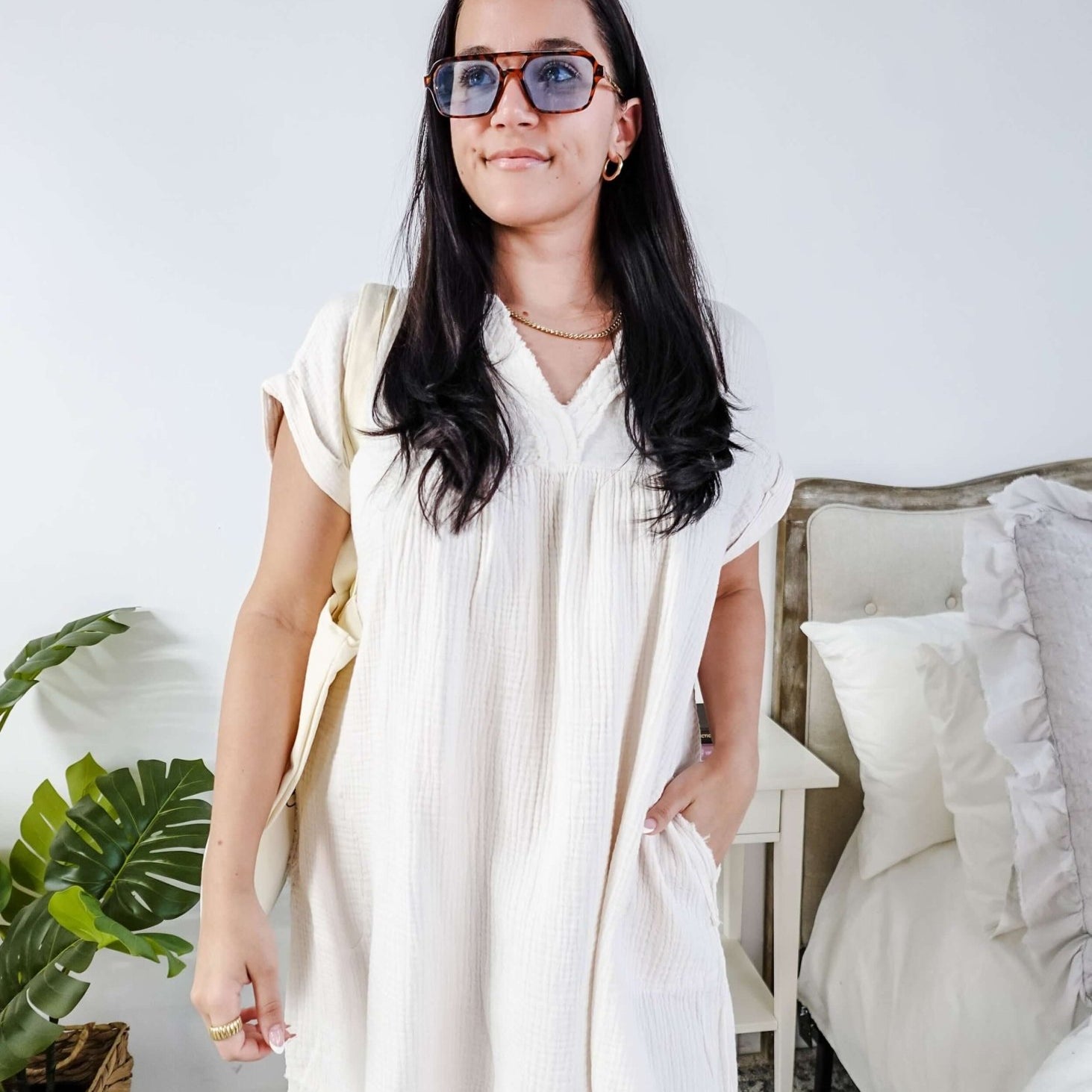 Woman wearing a white dress and sunglasses in a room with a plant and bed. Scarlett Ellie V-Neck Gauze Dress | Lightweight Summer Dress | Cloud Nine Pajamas