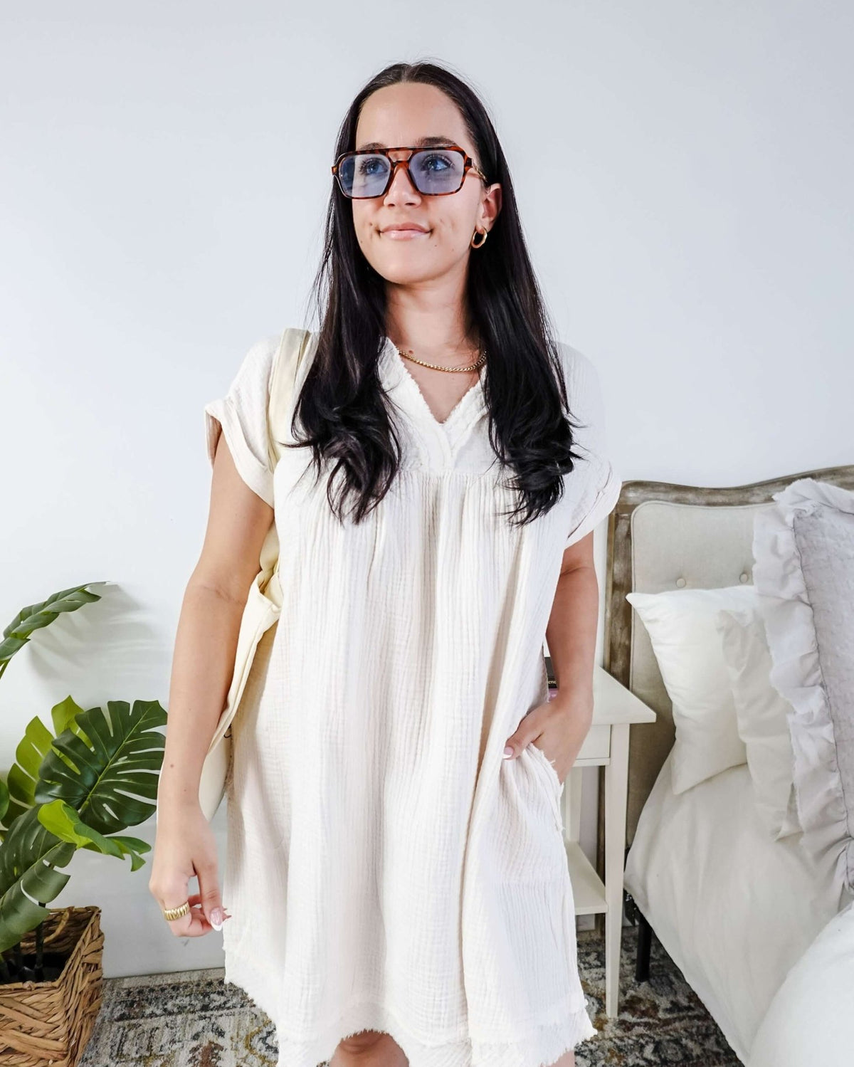 Woman wearing a white dress and sunglasses in a room with a plant and bed. Scarlett Ellie V-Neck Gauze Dress | Lightweight Summer Dress | Cloud Nine Pajamas