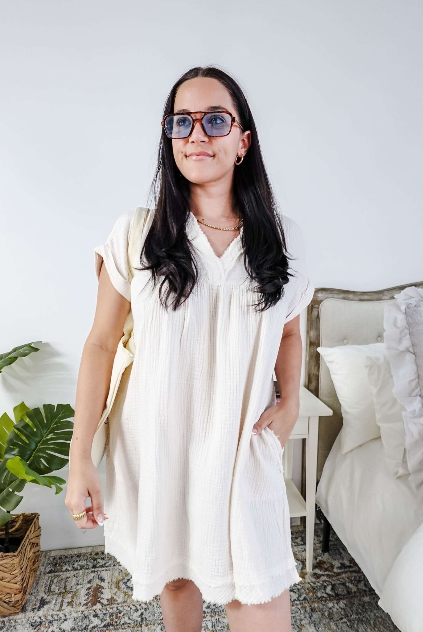 Woman wearing a white dress and sunglasses in a room with a plant and bed. Scarlett Ellie V-Neck Gauze Dress | Lightweight Summer Dress | Cloud Nine Pajamas