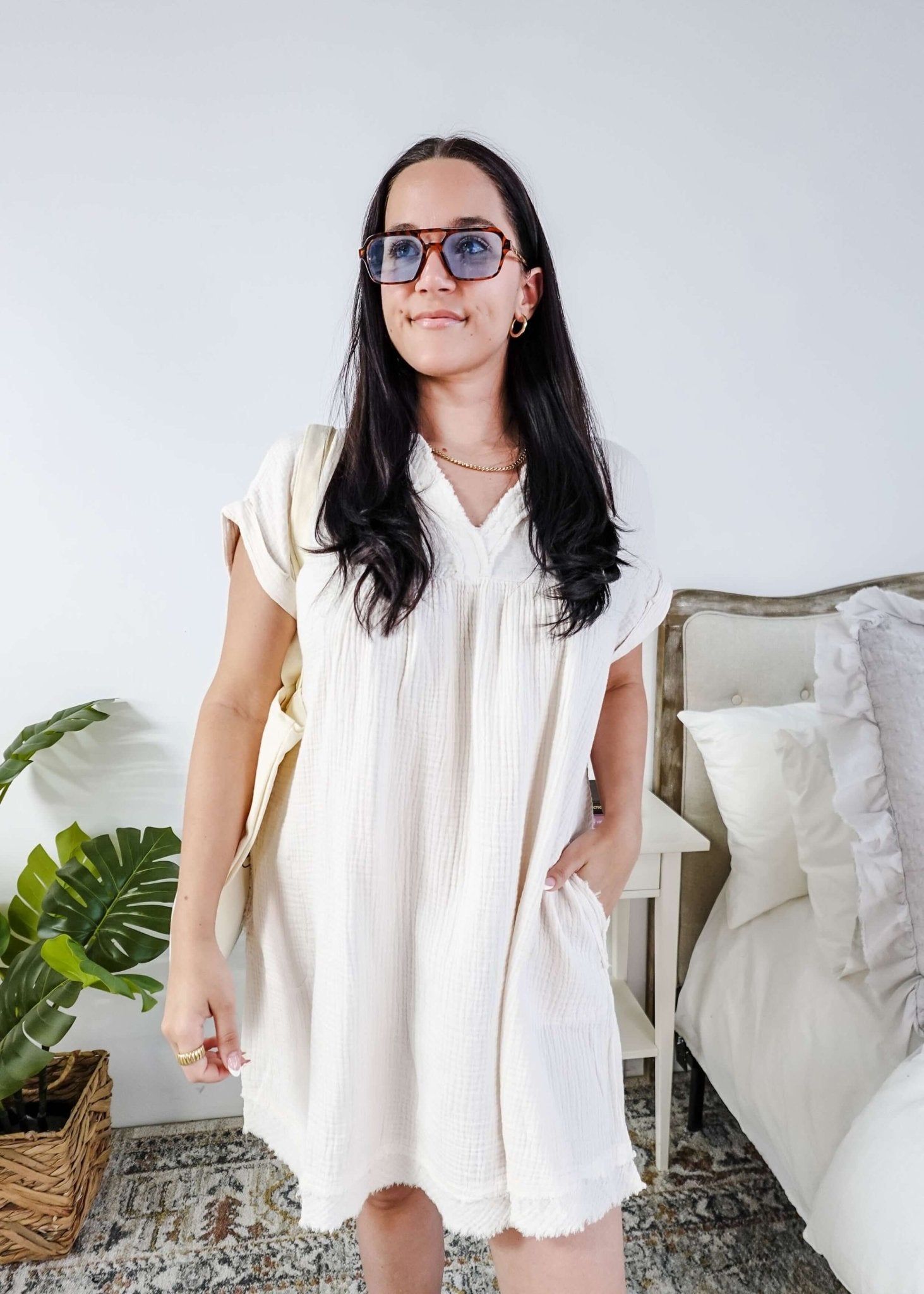 Woman wearing a white dress and sunglasses in a room with a plant and bed. Scarlett Ellie V-Neck Gauze Dress | Lightweight Summer Dress | Cloud Nine Pajamas