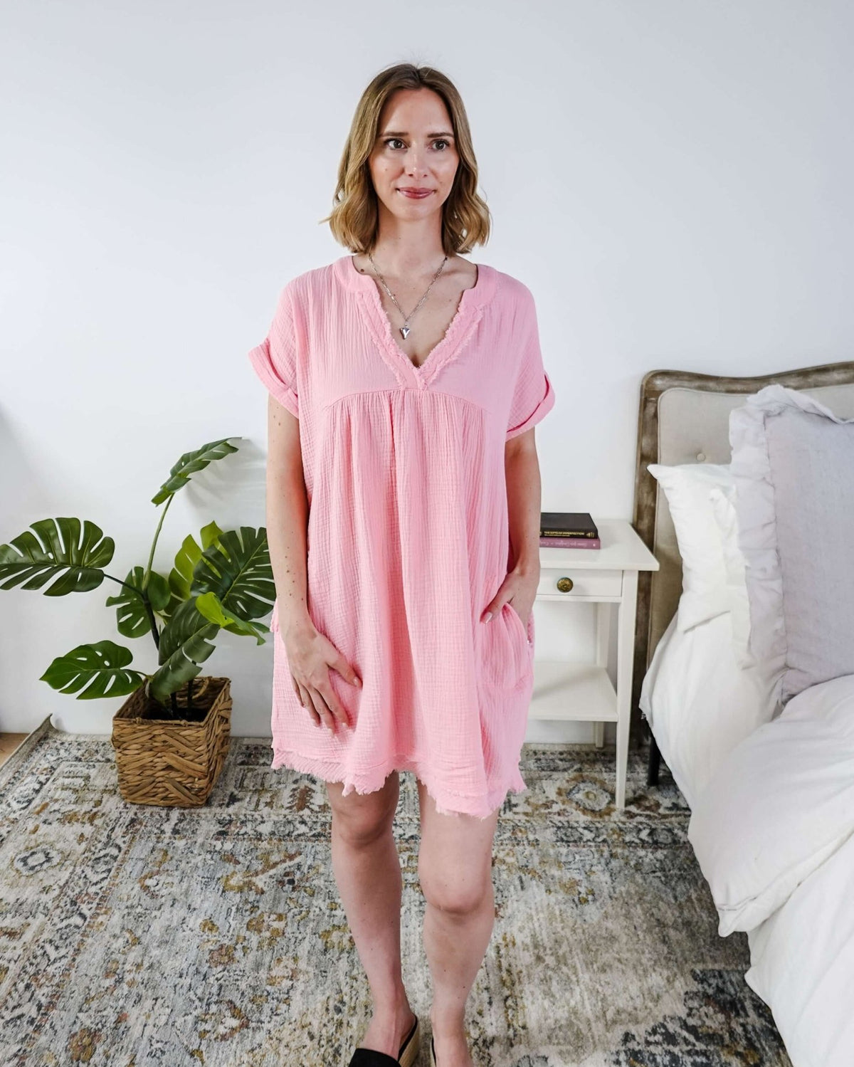 Scarlett Ellie V-Neck Gauze Dress | Lightweight Summer Dress | Cloud Nine Pajamas Woman wearing a pink dress standing in a bedroom with a plant and bed in the background.
