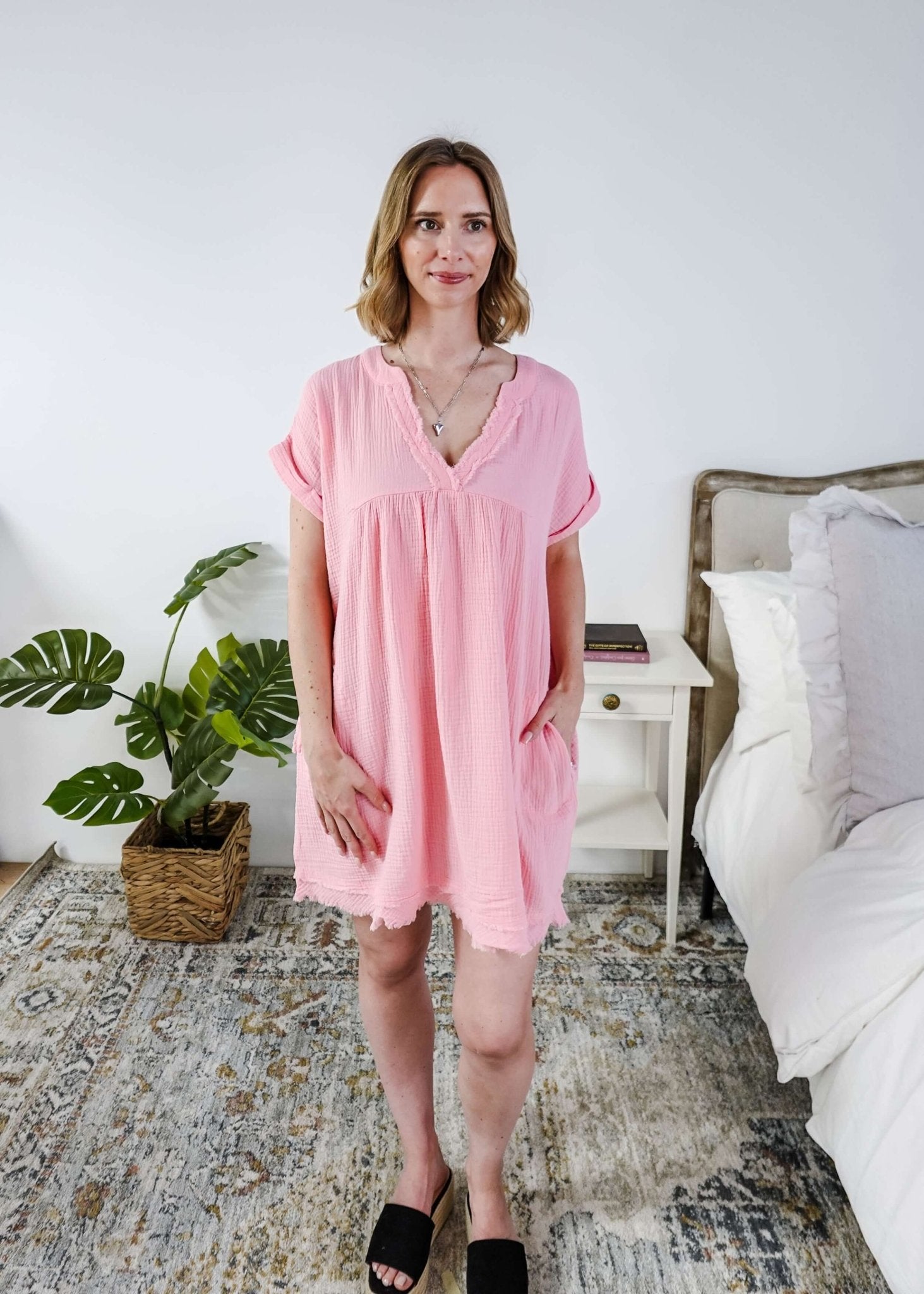 Scarlett Ellie V-Neck Gauze Dress | Lightweight Summer Dress | Cloud Nine Pajamas Woman wearing a pink dress standing in a bedroom with a plant and bed in the background.