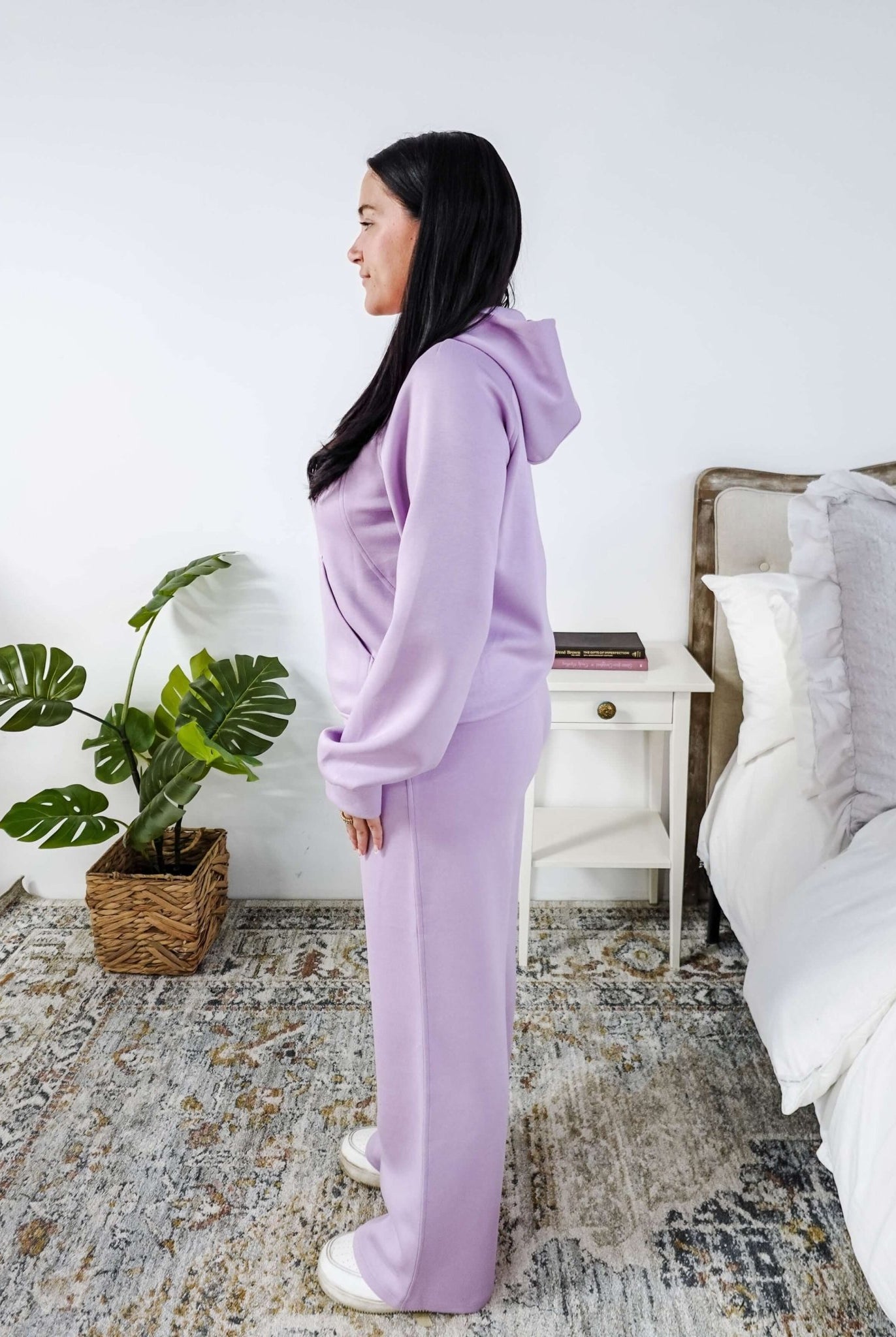 Person wearing a lavender tracksuit standing in a bedroom.