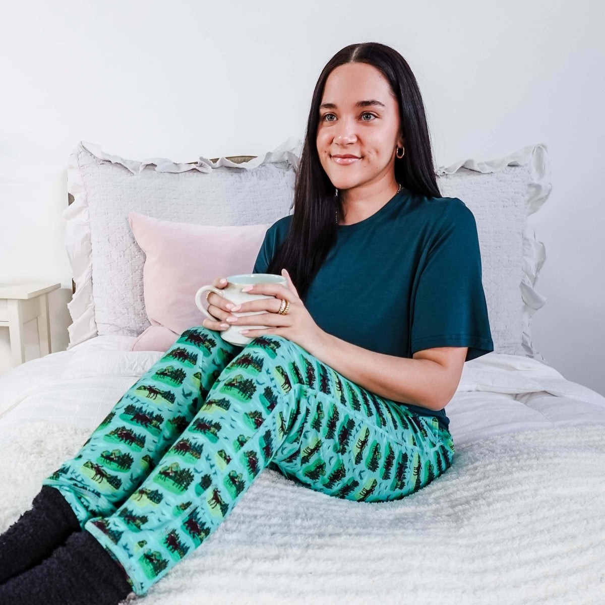 Person wearing Wildlife Aqua Unisex Bamboo Joggers by Bob's Sleepwear Co. while enjoying a drink on a bed.