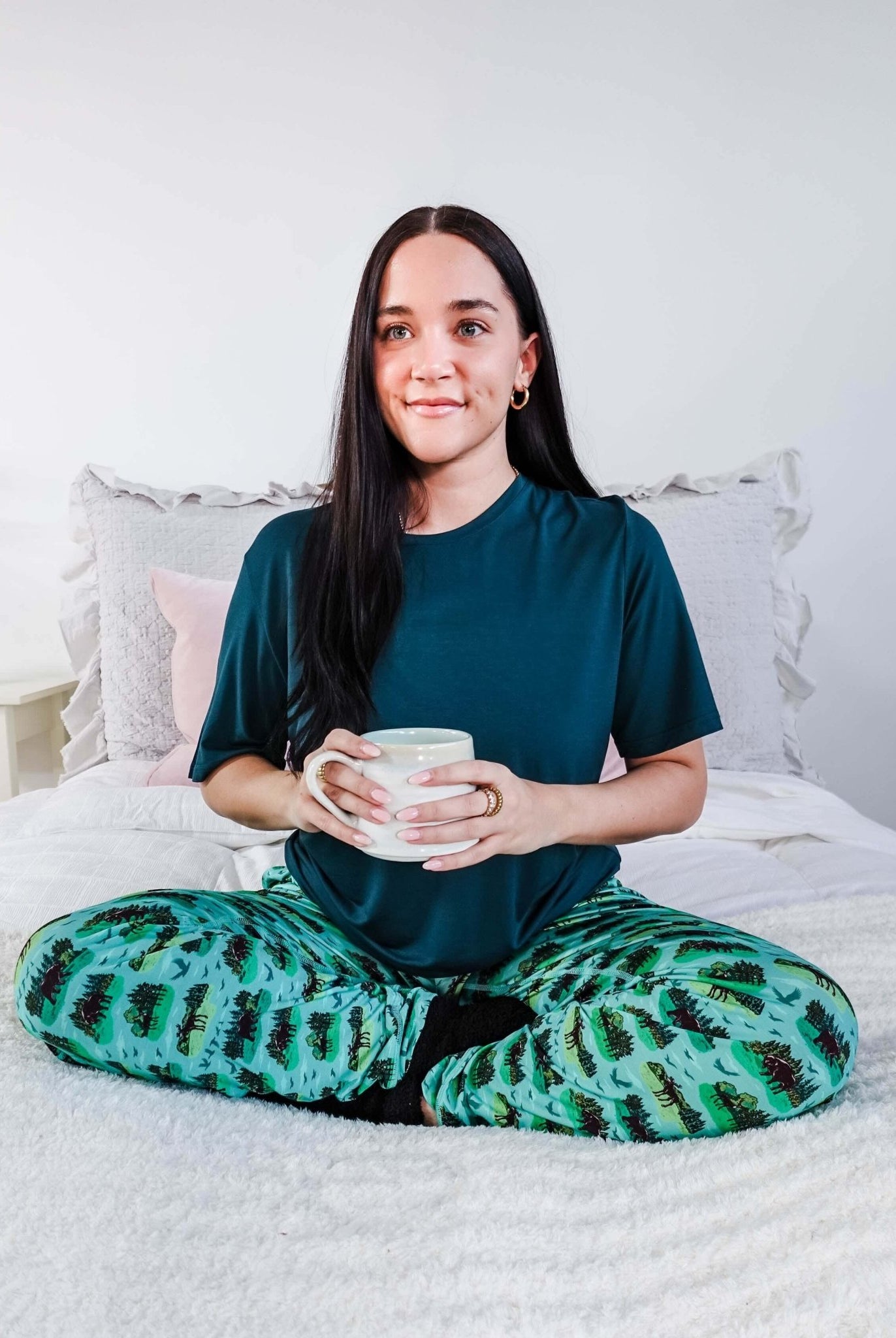 Model wearing Wildlife Aqua Unisex Bamboo Joggers while holding a cup, sitting on a bed.