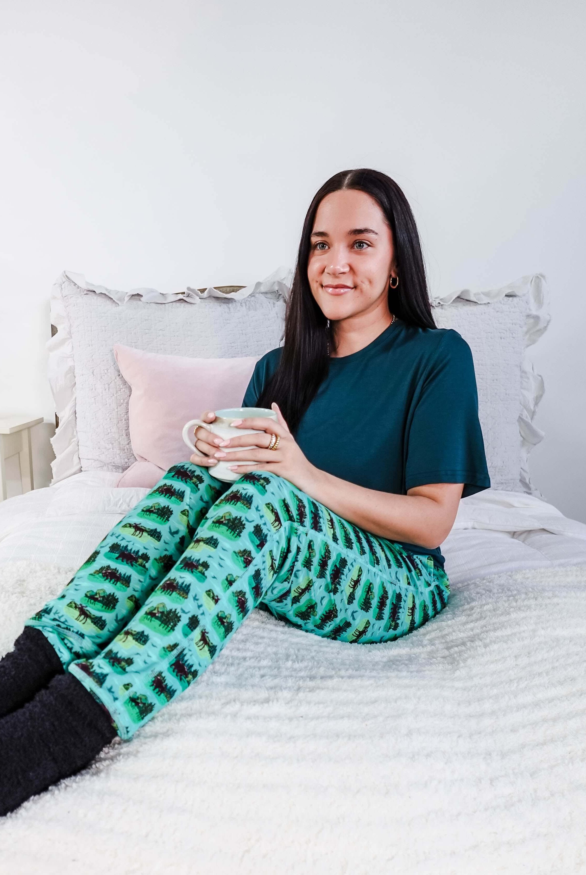 Person wearing Wildlife Aqua Unisex Bamboo Joggers by Bob's Sleepwear Co. while enjoying a drink on a bed.