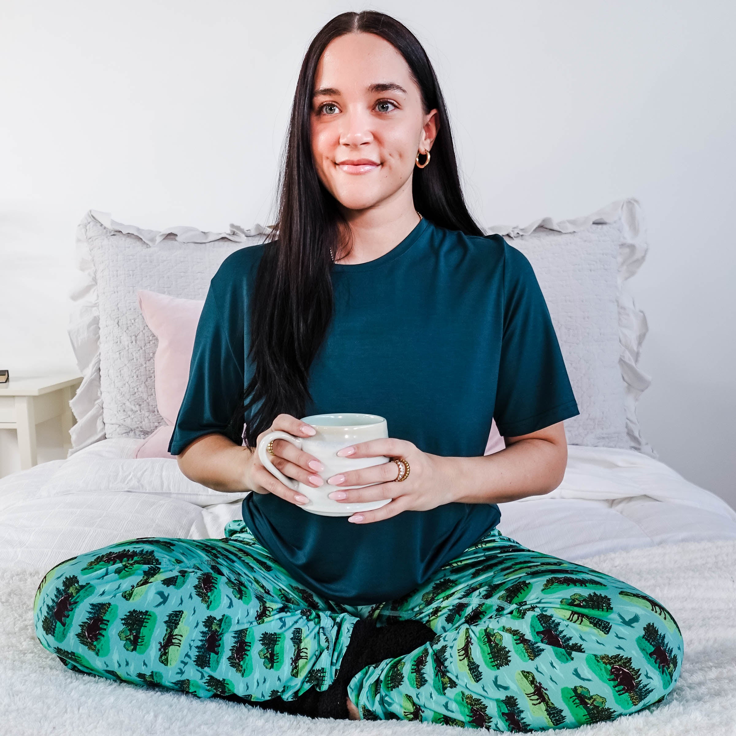 Model wearing Wildlife Aqua Unisex Bamboo Joggers while holding a cup, sitting on a bed.