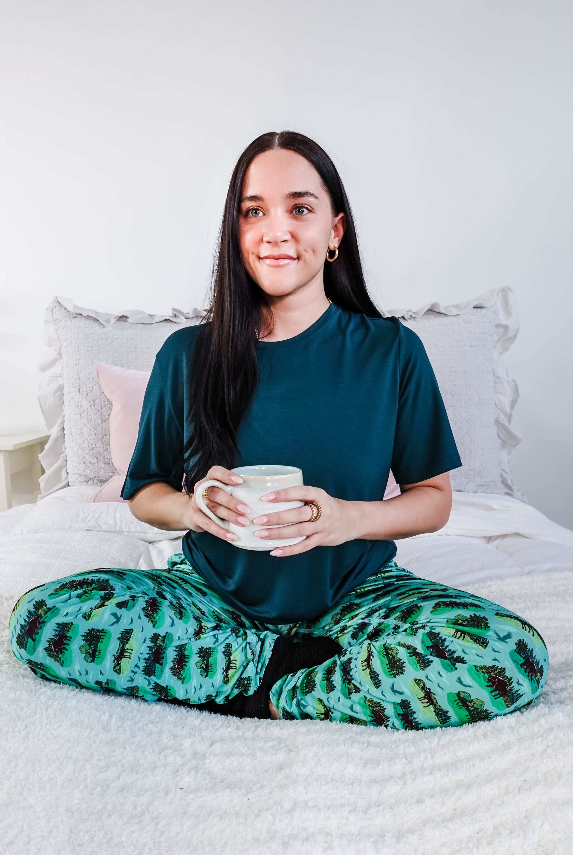 Model wearing Wildlife Aqua Unisex Bamboo Joggers while holding a cup, sitting on a bed.