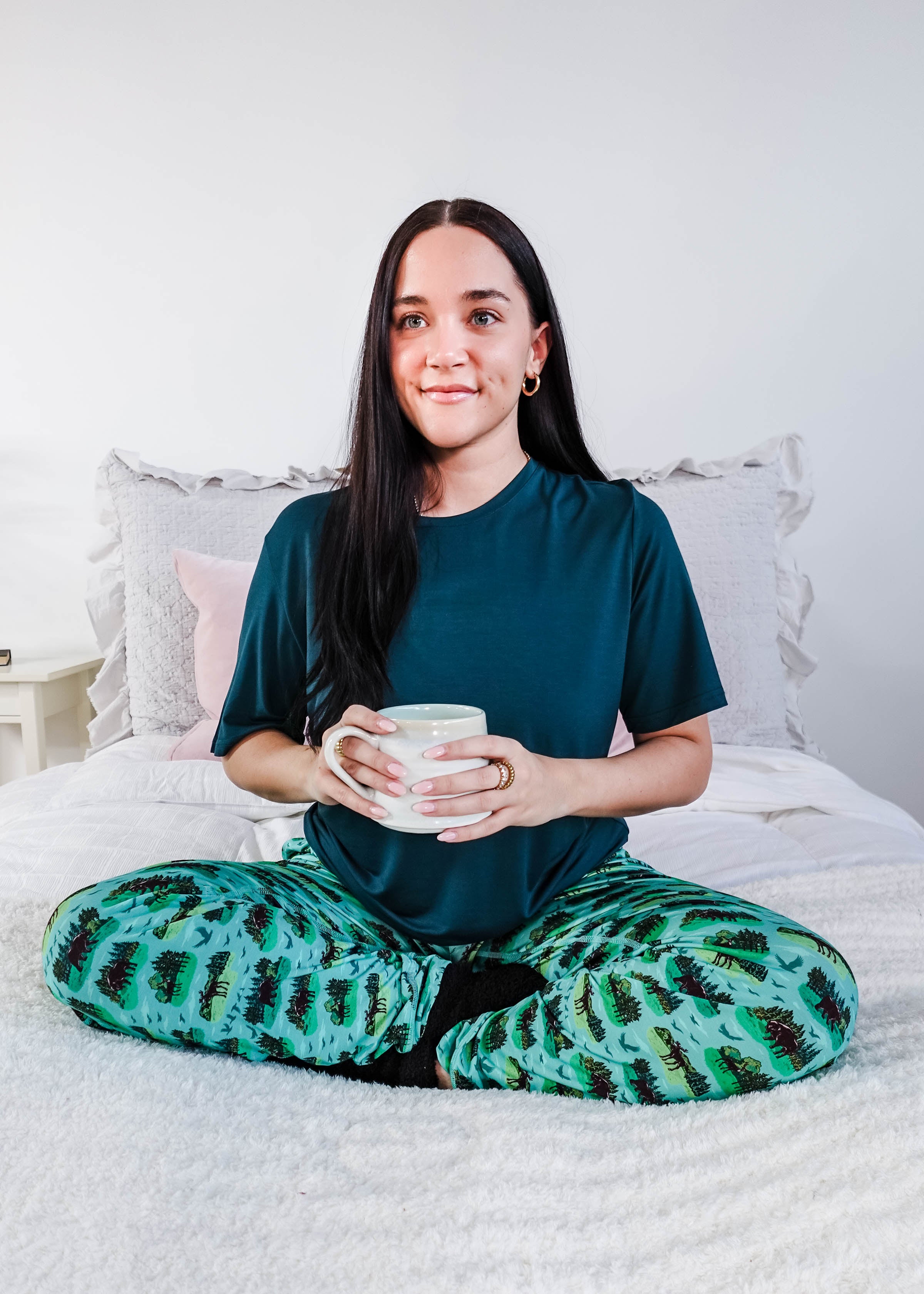 Model wearing Wildlife Aqua Unisex Bamboo Joggers while holding a cup, sitting on a bed.