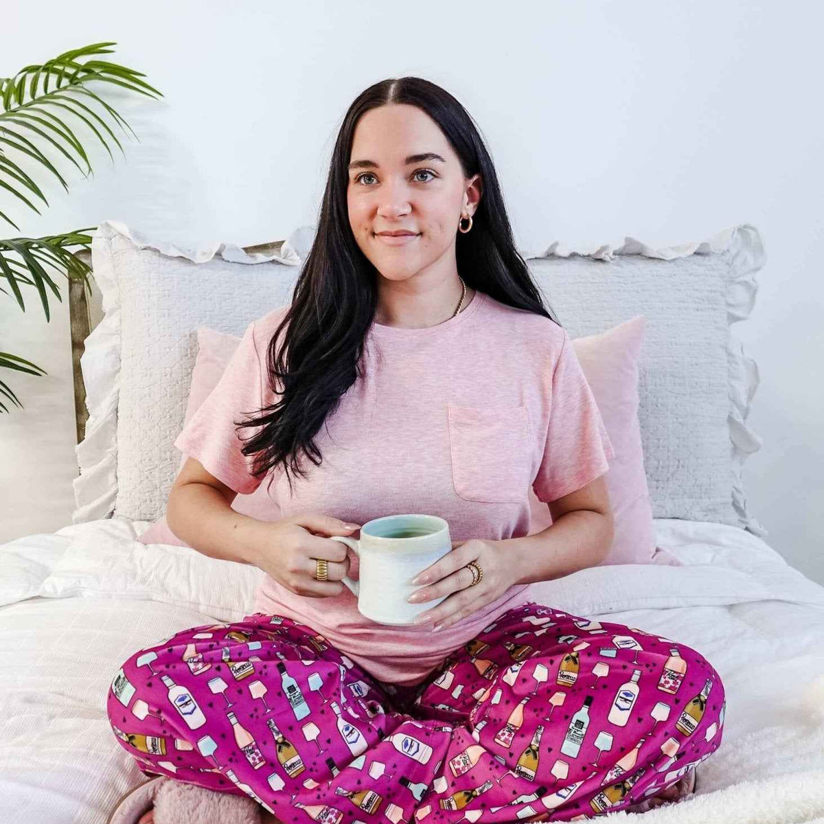 Sydney wearing the Wine Down velvety velour pajama set featuring hot pink wine print pants and a light pink pocket tee.
