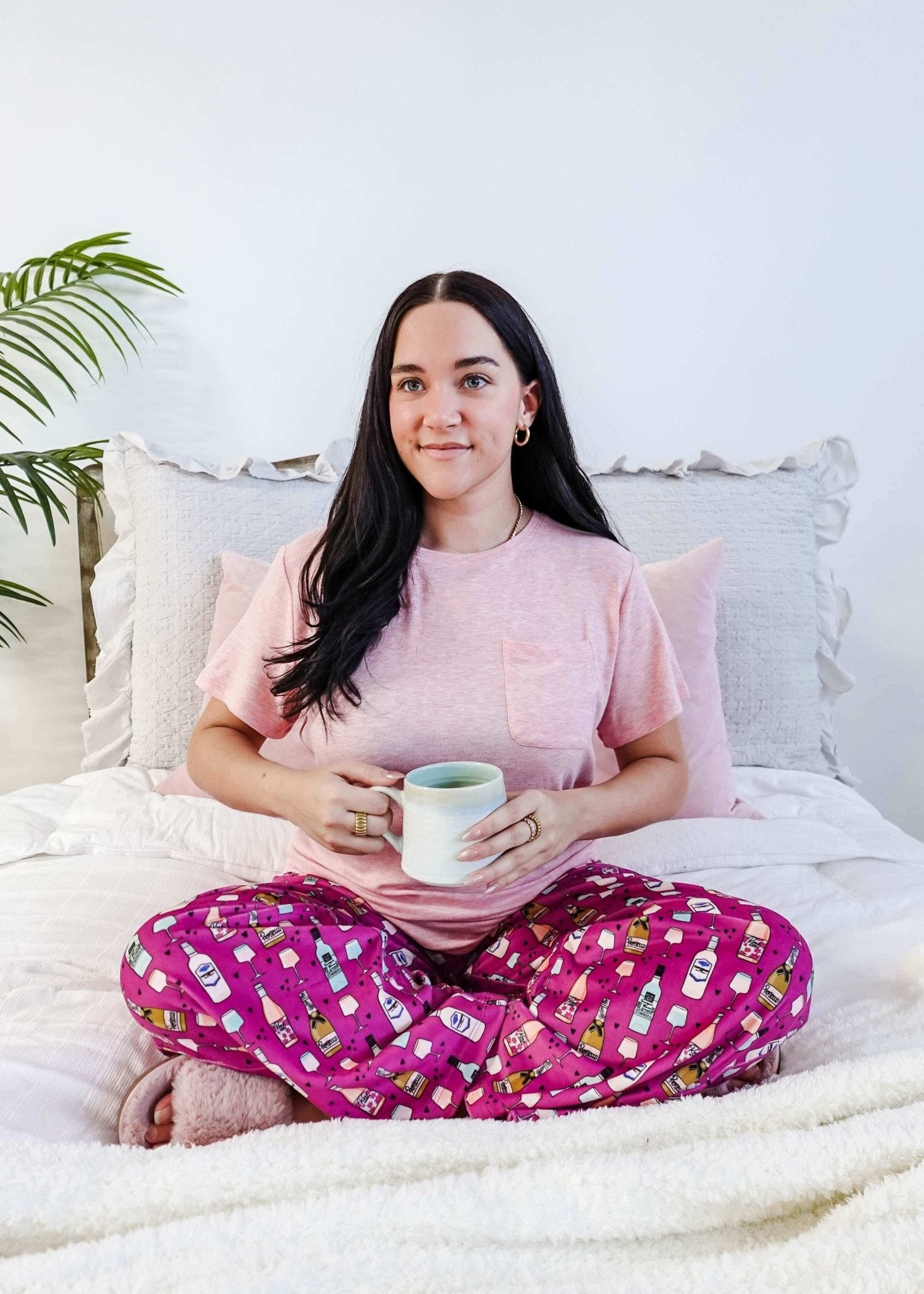 Sydney wearing the Wine Down velvety velour pajama set featuring hot pink wine print pants and a light pink pocket tee.
