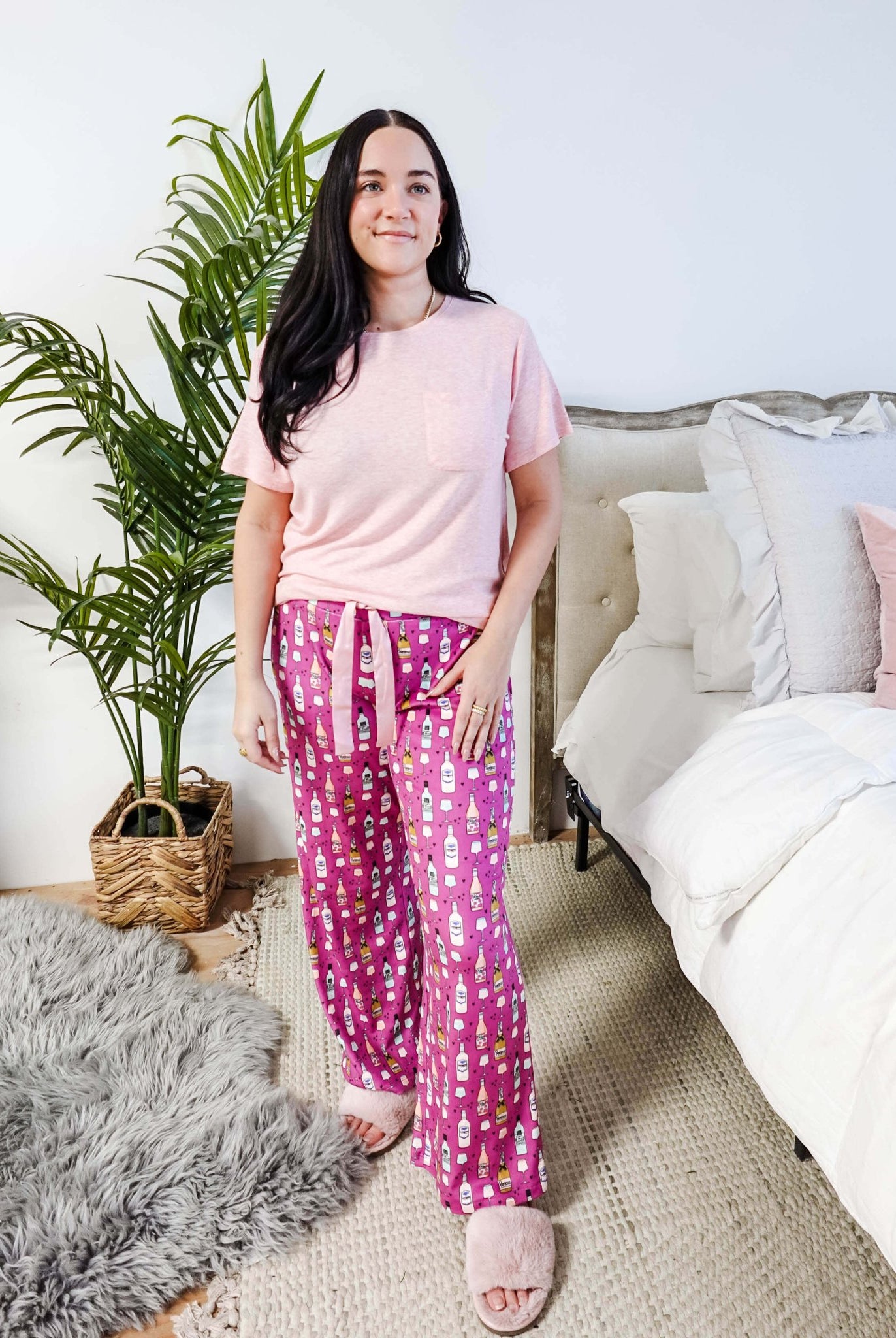 Sydney wearing the Wine Down velvety velour pajama set featuring hot pink wine print pants and a light pink pocket tee.