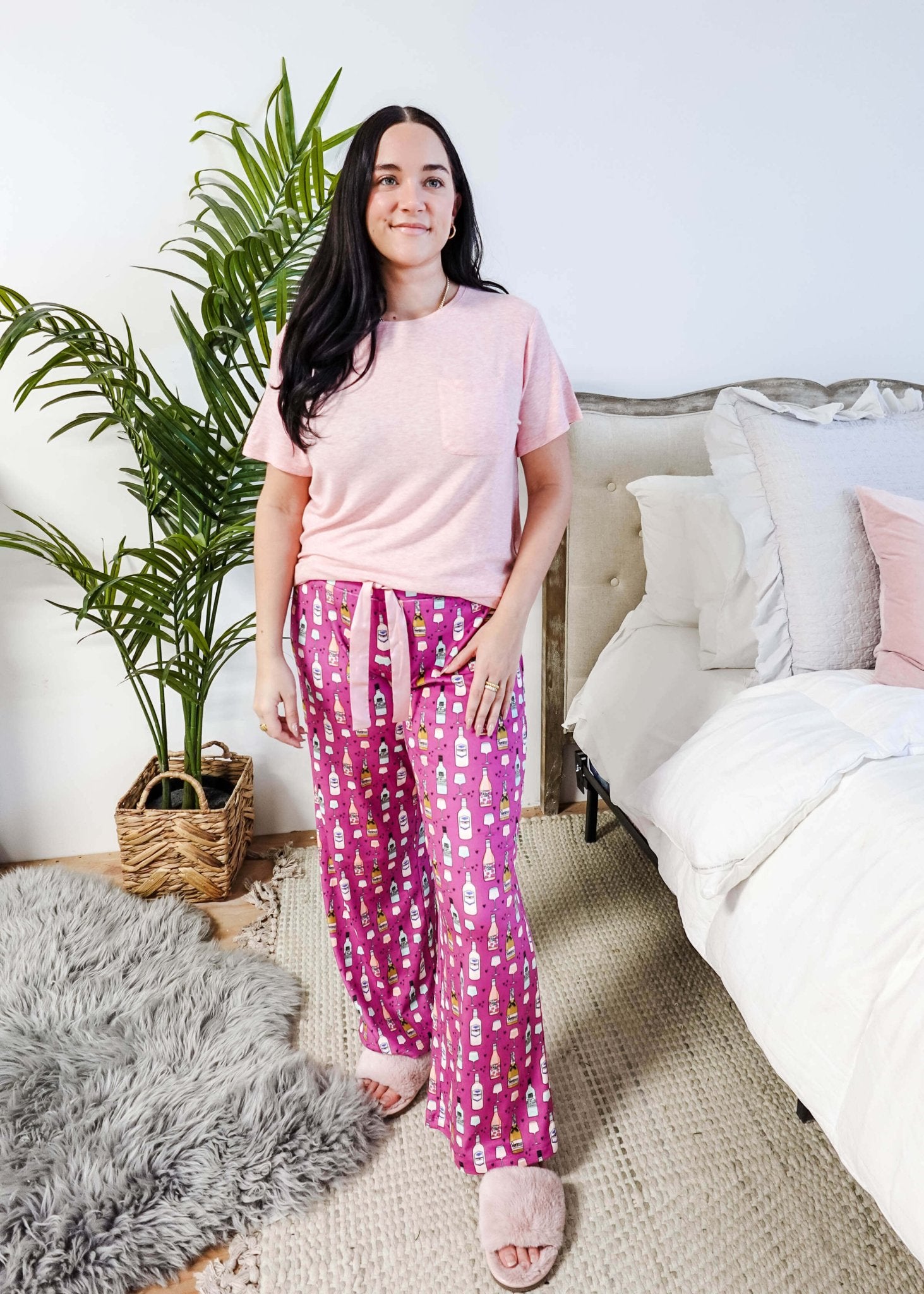 Sydney wearing the Wine Down velvety velour pajama set featuring hot pink wine print pants and a light pink pocket tee.