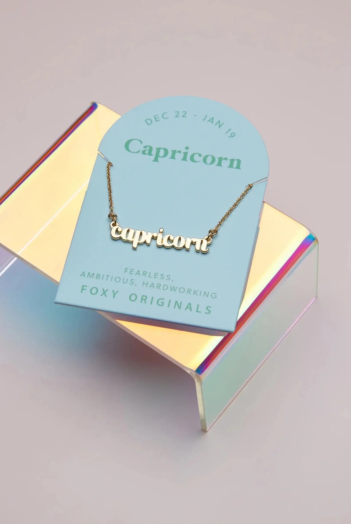 Zodiac Script Necklace in 14K Plated Gold displayed on a holographic stand with Capricorn card.