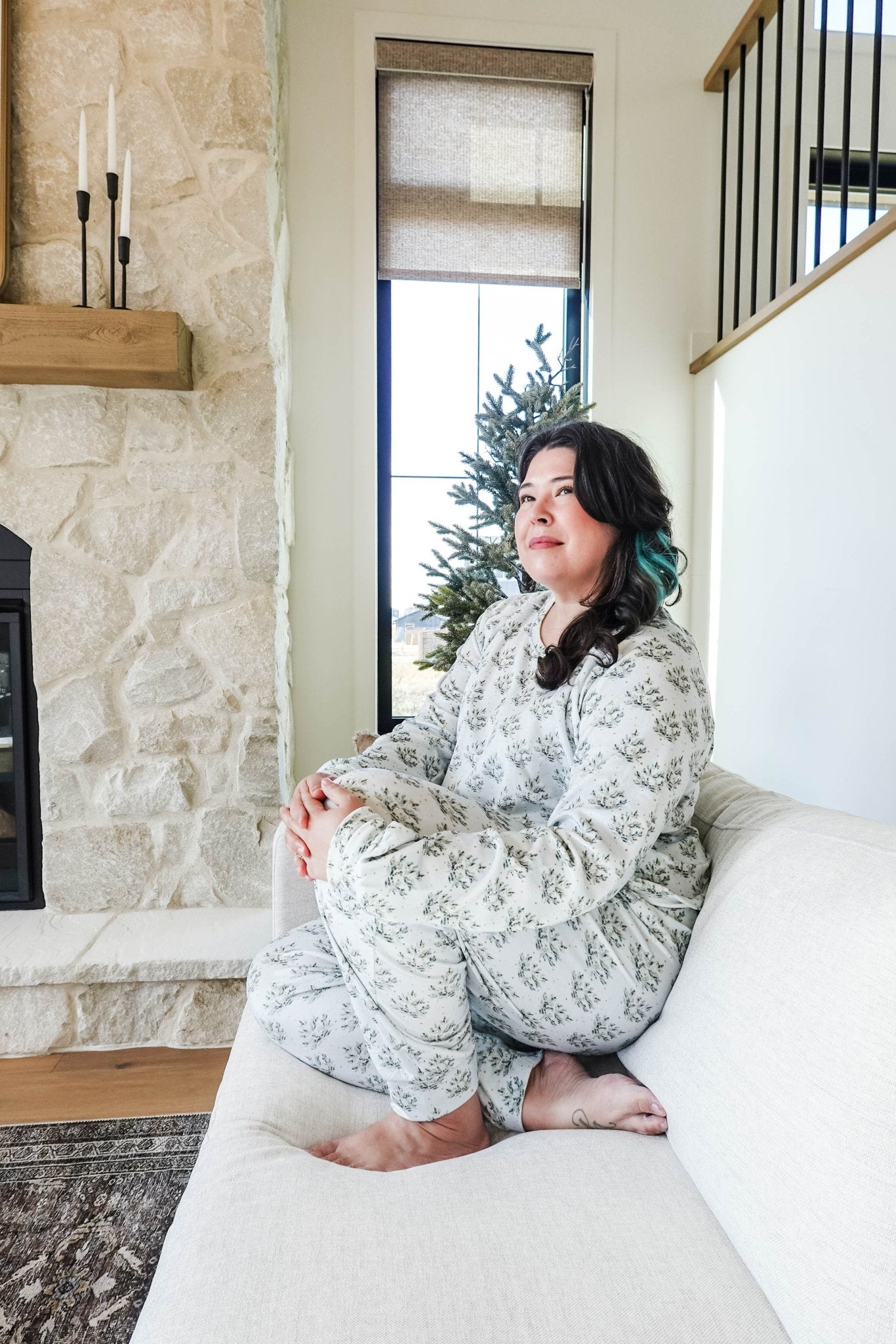 Woman sitting in cozy Miranda Nic Loungewear in a stylish living room with a fireplace and a Christmas tree.