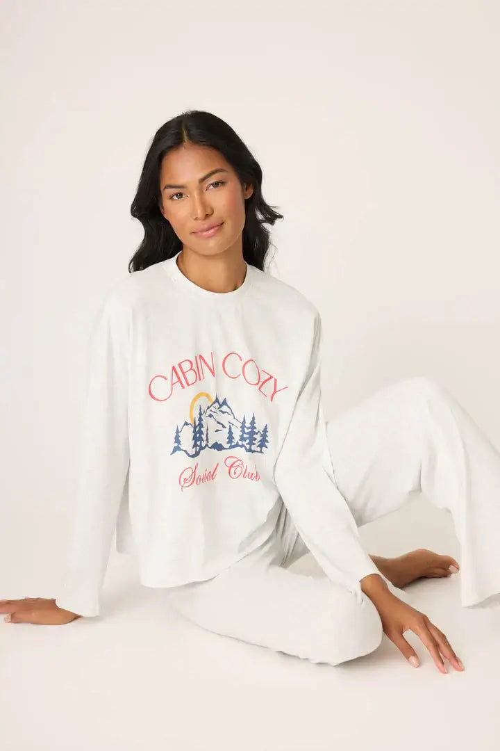 Model Candy wearing the PJ Salvage Cabin Cozy Long Sleeve Lounge Set in cloud white. She is wearing the cropped long sleeve top and relaxed drawstring pants, showing the "Cabin Cozy Social Club" graphic.