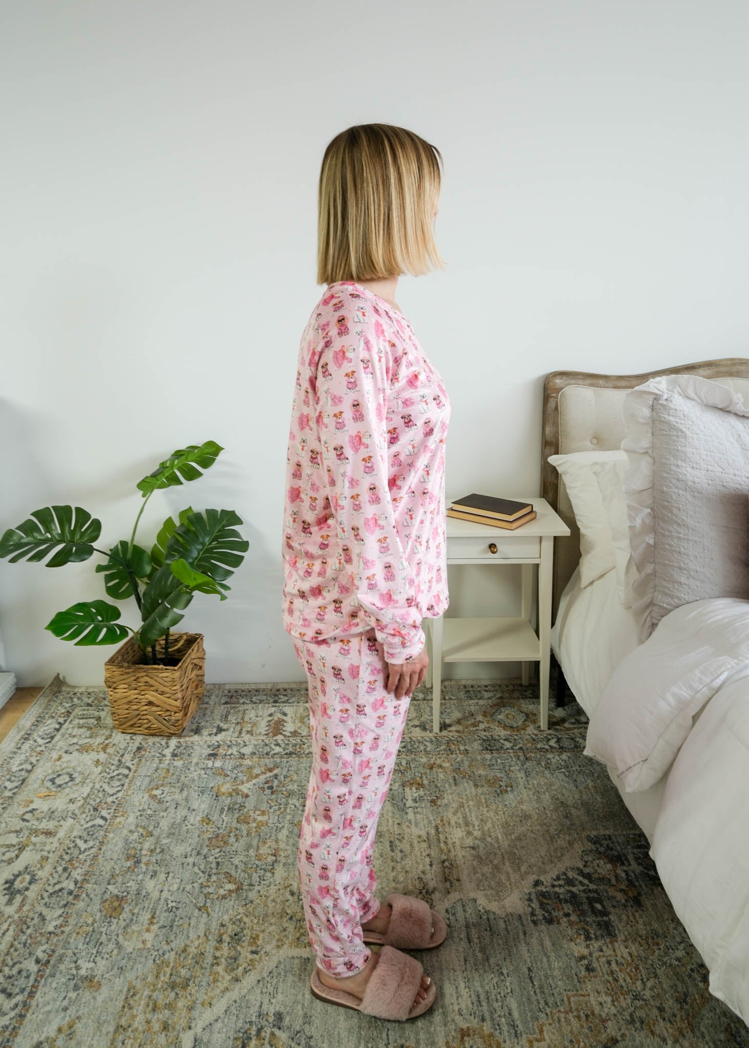 Side profile on model in bedroom of Miranda Nic women's pink velour long sleeve top and jogger pants loungewear set featuring Chic Puppies dog print - Cloud Nine Pajamas