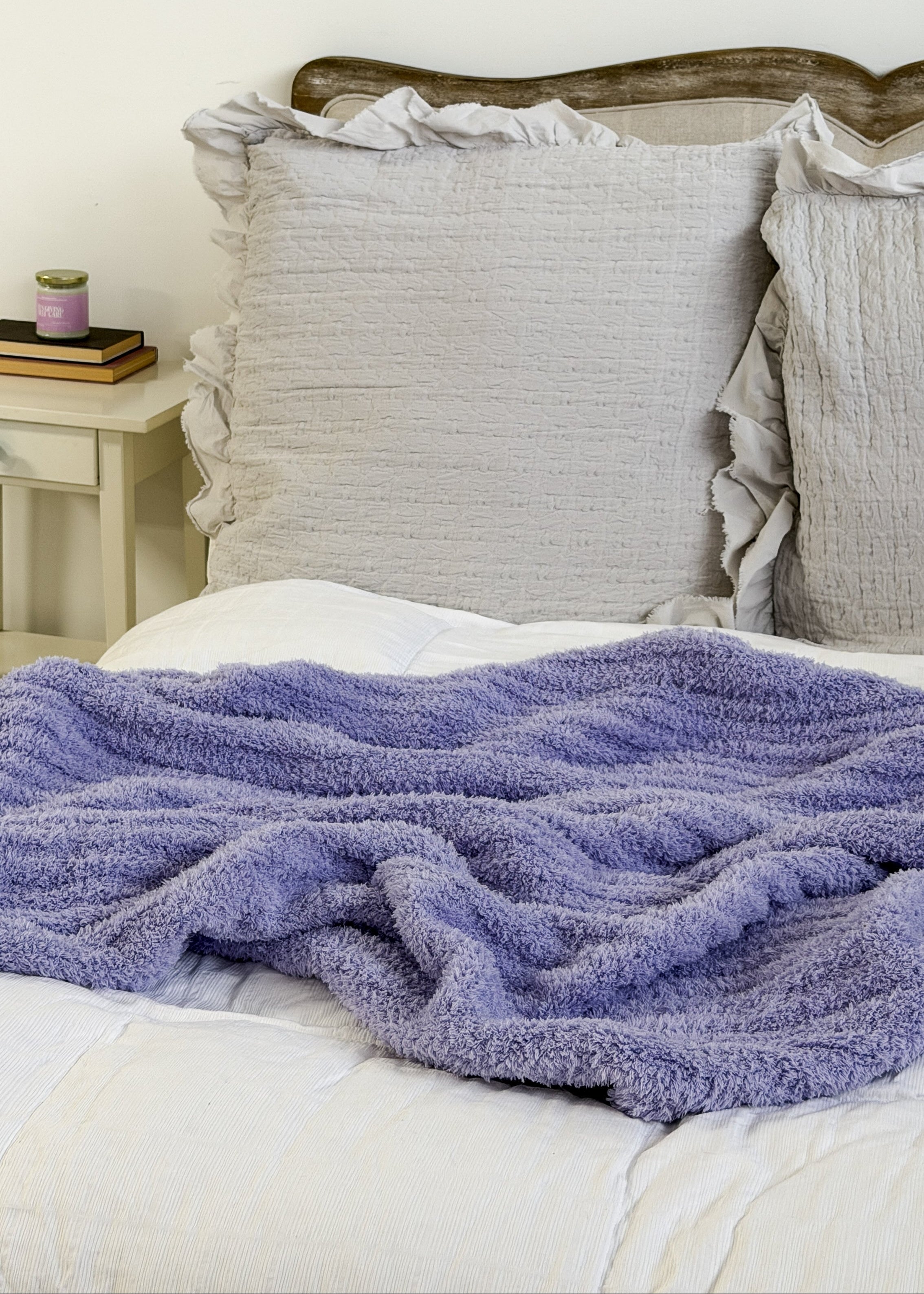 lavender plush cozy cabin blanket lounge by jan marie Bed with a purple blanket and gray pillows against a white wall.