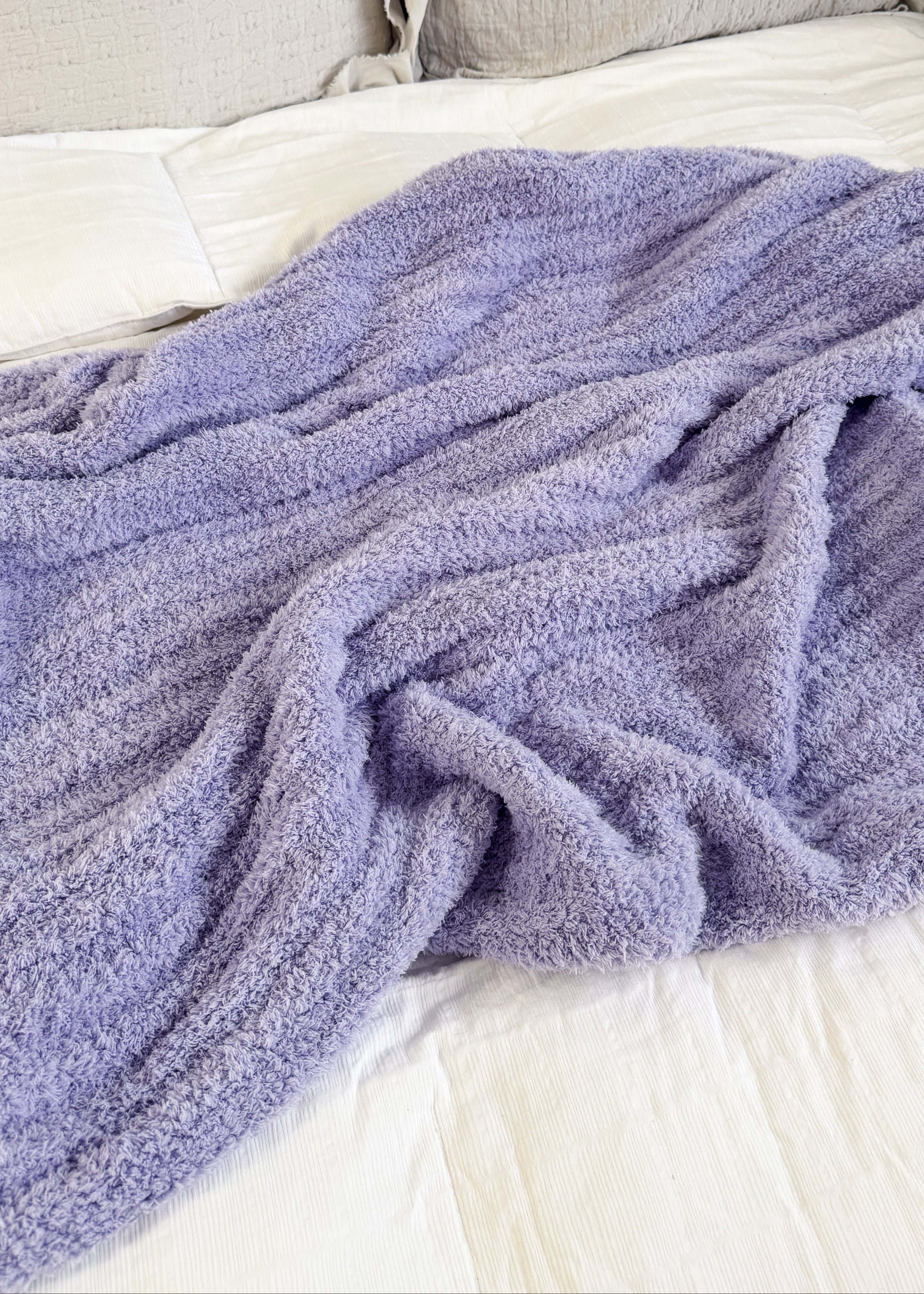 Purple blanket draped over a bed with beige pillows