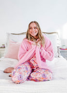 Essential Hooded Fluffy Cozy Cardigan with Pockets worn by a smiling woman sitting on a bed.