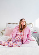 Model wearing the Essential Hooded Fluffy Cozy Cardigan with Pockets, seated on a bed in cozy loungewear.
