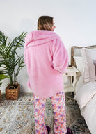 Woman wearing an Essential Hooded Fluffy Cozy Cardigan with Pockets in pink, standing in a cozy bedroom.