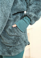 Close-up of a person wearing a plush, textured dark teal fleece cardiganwith a matching ribbed knit cuff and dark midnight teal bamboo pajama pants, with a hand in a pocket. Cloud Nine Pajamas Edmonton 