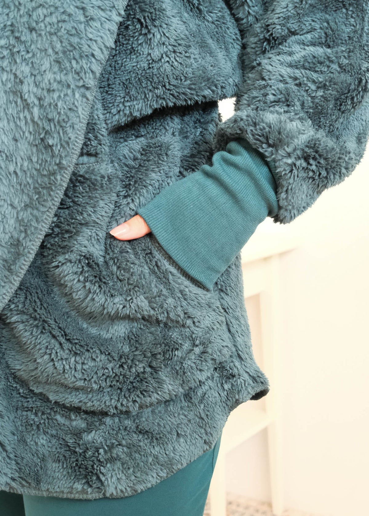 Close-up of a person wearing a plush, textured dark teal fleece cardiganwith a matching ribbed knit cuff and dark midnight teal bamboo pajama pants, with a hand in a pocket. Cloud Nine Pajamas Edmonton 