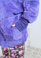 Close-up of a woman wearing the purple fluffy hooded cardigan by Jan Marie  open over a black top, showing the plush sherpa-like texture, wide lapel, and pruple ribbed cuff at the wrist with one hand tucked into the front pocket. Cloud Nine Pajamas Edmonton 