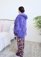 Close-up detail of the Jan Marie Fluffy hooded cardigan's deep front pocket in purple plush fabric, with a hand tucked inside and the purple ribbed cuff visible, floral pajama pants underneath. Cloud Nine Pajamas Edmonton